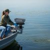 Female applicator applying gray colored granules to lake via boat mounted spreader.
