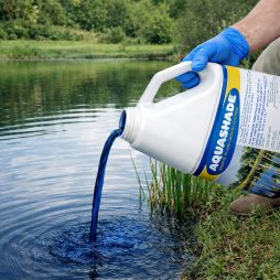 Gloved applicator pouring Aquashade from the jug along the shoreline of a contained pond.
