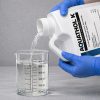 Aquathol K being poured into a graduated beaker for precise measurement before application.