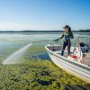 Professional female applicator sprays liquid aquatic treatment to lake water with boat mounted Ironvale sprayer.