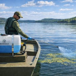 Boat-mounted sprayer applying Cutrine Plus liquid algaecide to floating lake algae near the shoreline.