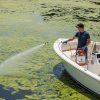 Professional male applicator sprays liquid aquatic treatment to lake water with boat mounted Ironvale sprayer.