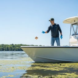 Professional male applicator tosses NT-MAX Clarifier Lake Pond Sludge Muck Digester to lake from boat.-lake.