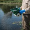 Technician using Ironvale hand spreader applying aquatic granules over a treatment area.