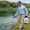 Applicator wearing long sleeves and blue nitrile gloves spraying aquatic product into pond along shoreline with handheld pump sprayer